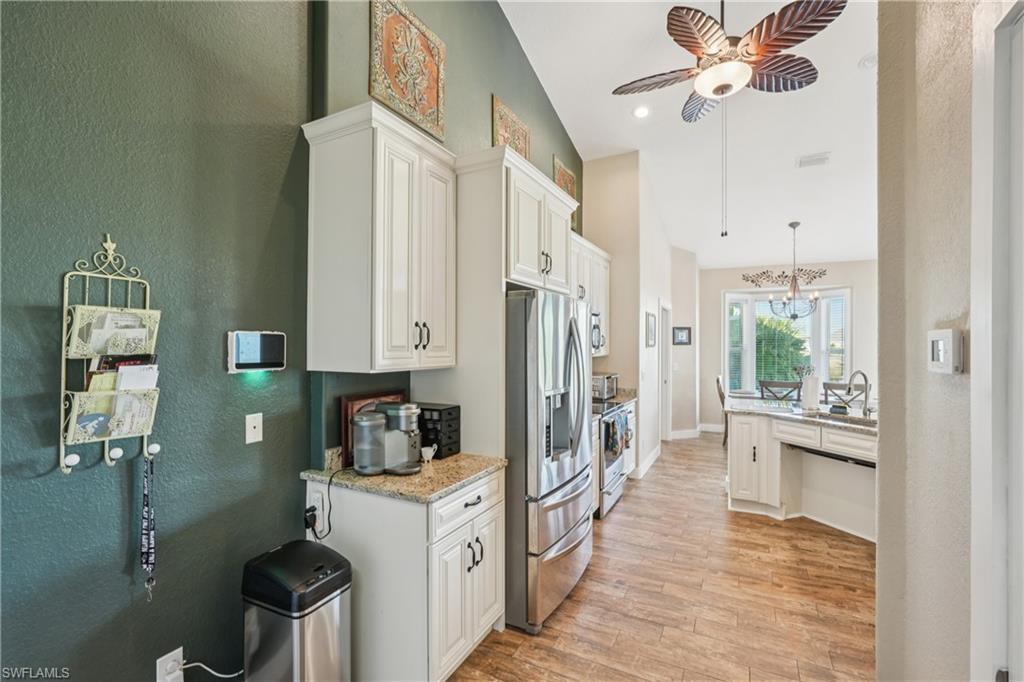 Kitchen with decorative light fixtures, a textured wall, stainless steel appliances, light stone countertops, and high vaulted ceiling