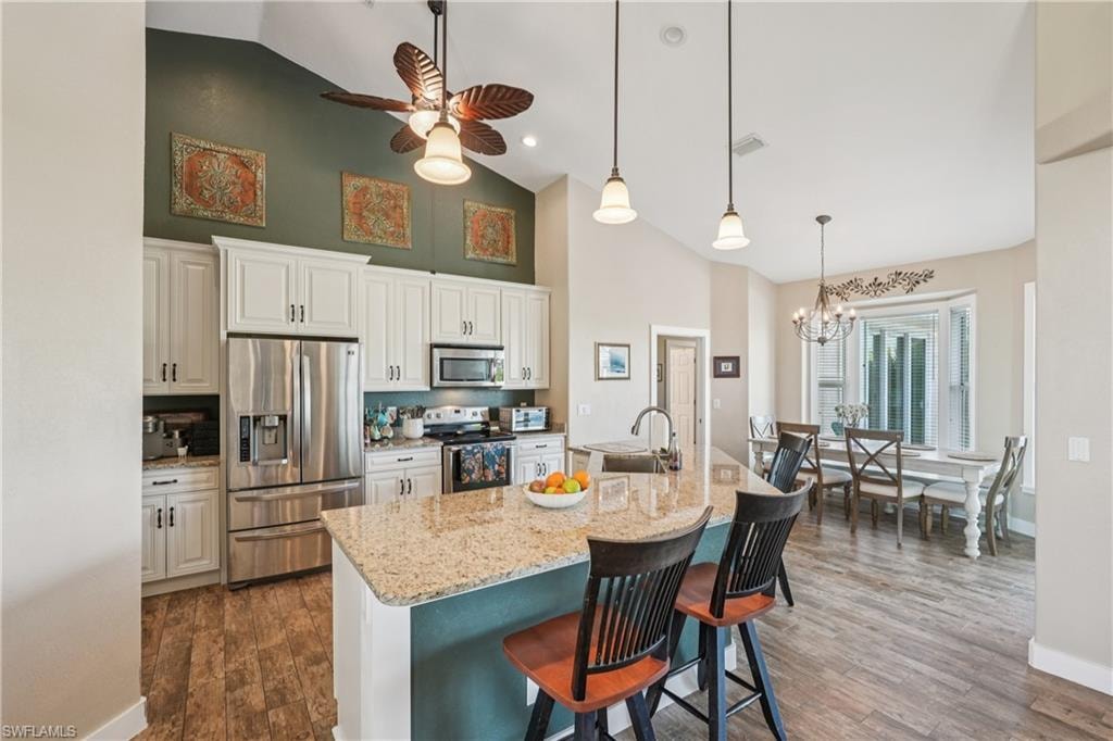 Kitchen with stainless steel appliances, a kitchen bar, hanging light fixtures, ceiling fan, and light stone countertops