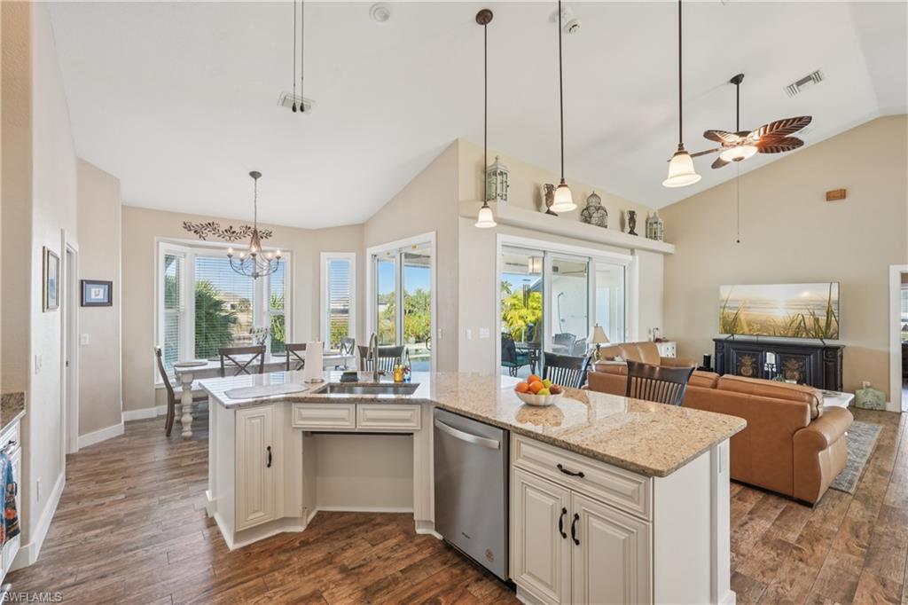 Kitchen featuring lofted ceiling, light stone counters, hanging light fixtures, dishwasher, and a kitchen island with sink