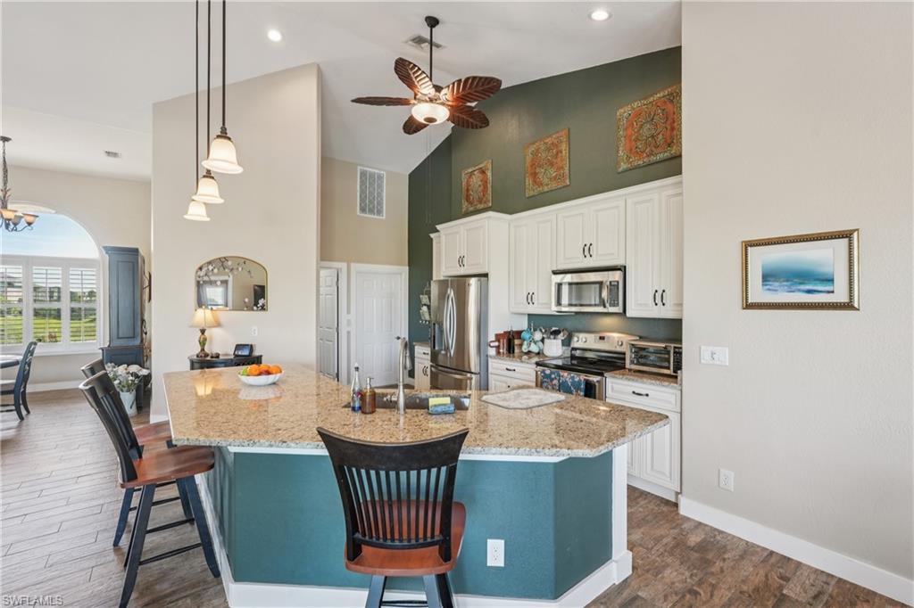 Kitchen featuring a breakfast bar area, high vaulted ceiling, light stone counters, appliances with stainless steel finishes, and white cabinetry