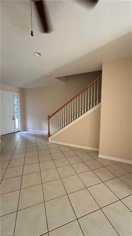 Unfurnished living room featuring stairs, light tile patterned flooring, and a ceiling fan
