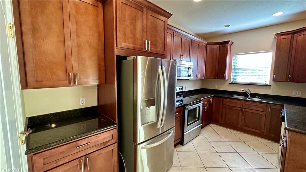 Kitchen featuring appliances with stainless steel finishes, dark stone countertops, light tile patterned floors, brown cabinetry, and recessed lighting