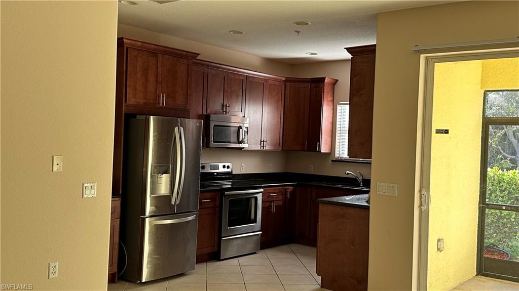 Kitchen with appliances with stainless steel finishes, light tile patterned floors, dark stone countertops, dark brown cabinetry, and a textured wall