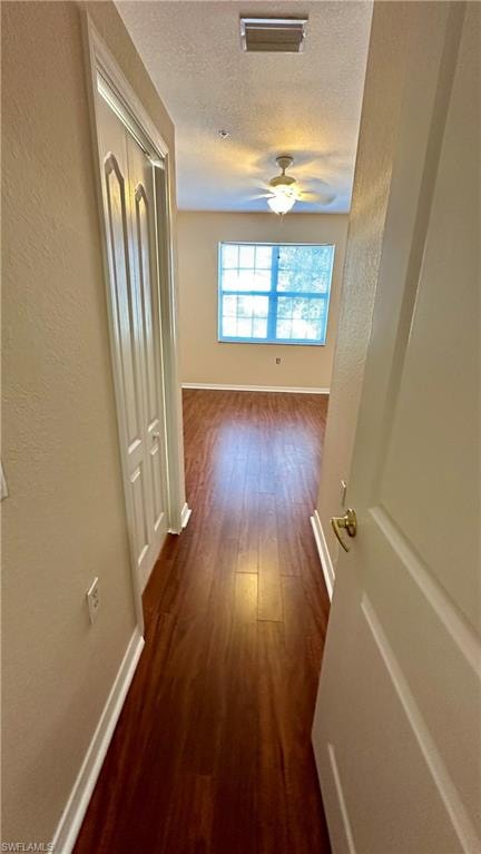 Corridor with dark wood finished floors, a textured wall, and a textured ceiling