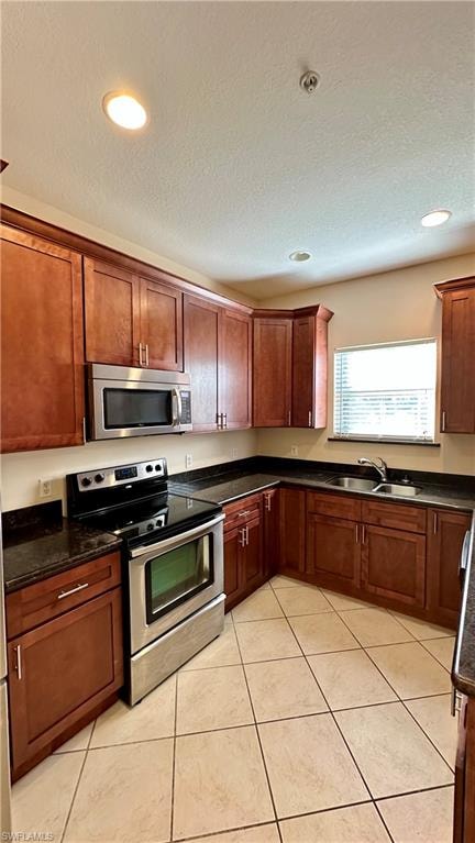 Kitchen with appliances with stainless steel finishes, dark stone countertops, a textured ceiling, recessed lighting, and light tile patterned floors