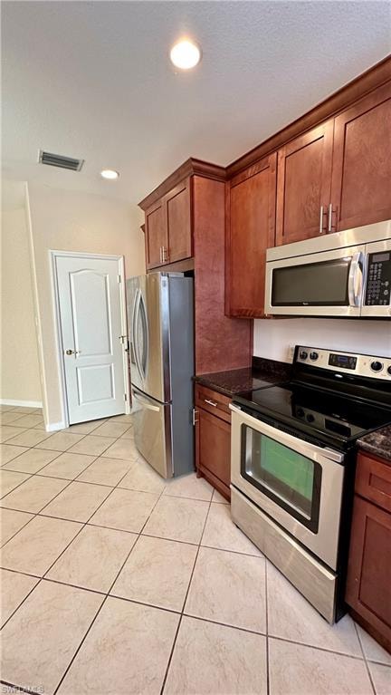 Kitchen featuring stainless steel appliances, recessed lighting, light tile patterned floors, dark stone counters, and brown cabinets