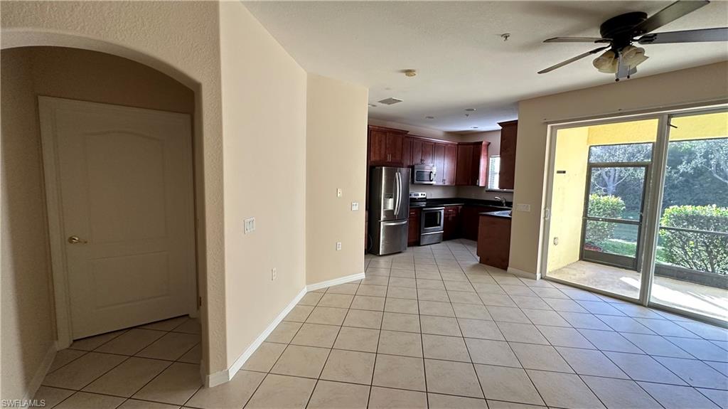 Kitchen with arched walkways, appliances with stainless steel finishes, dark countertops, ceiling fan, and light tile patterned floors