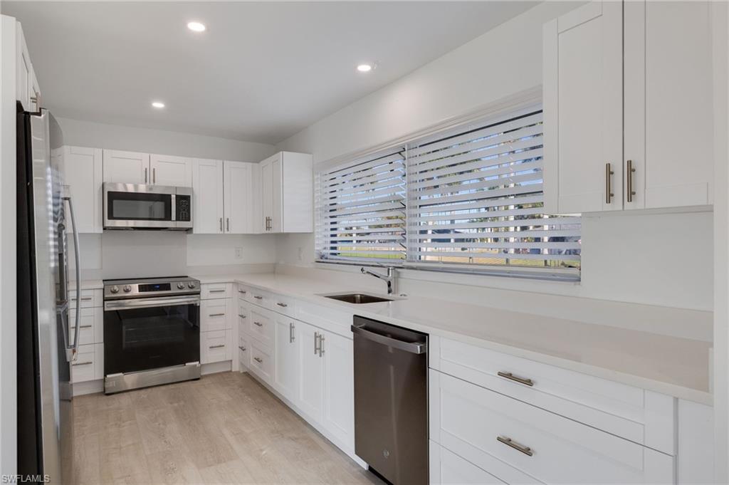 Kitchen featuring stainless steel appliances, white cabinets, light wood-style floors, recessed lighting, and light stone countertops