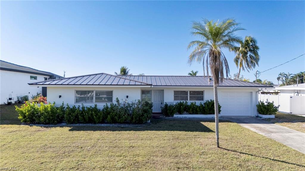 Ranch-style home featuring a garage, a front lawn, a metal roof, and concrete driveway