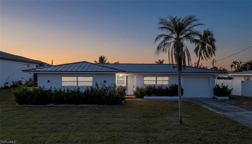 View of front of property with a metal roof, an attached garage, concrete driveway, and a yard