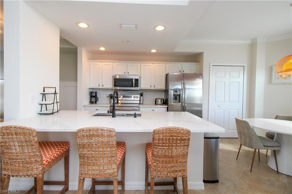 Kitchen featuring a kitchen bar, appliances with stainless steel finishes, white cabinetry, and sink