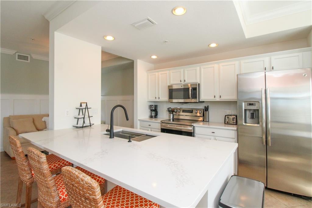 Kitchen featuring a kitchen bar, white cabinetry, sink, and appliances with stainless steel finishes