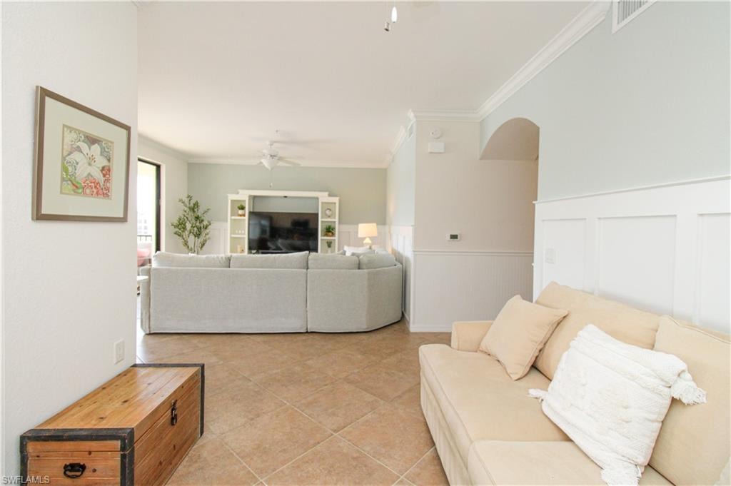 Living room featuring ceiling fan, light tile patterned floors, and crown molding