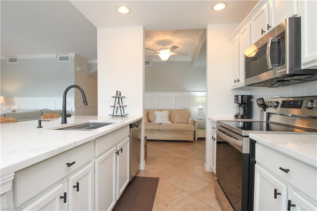 Kitchen with sink, light stone countertops, light tile patterned floors, appliances with stainless steel finishes, and white cabinetry