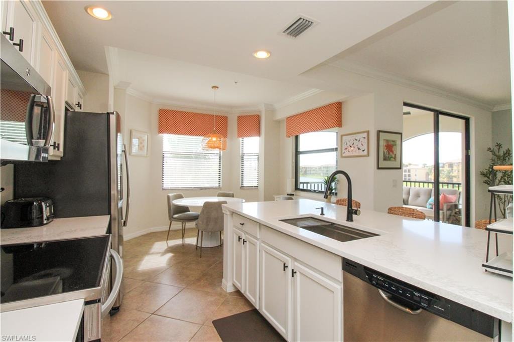 Kitchen featuring a wealth of natural light, sink, decorative light fixtures, white cabinets, and appliances with stainless steel finishes