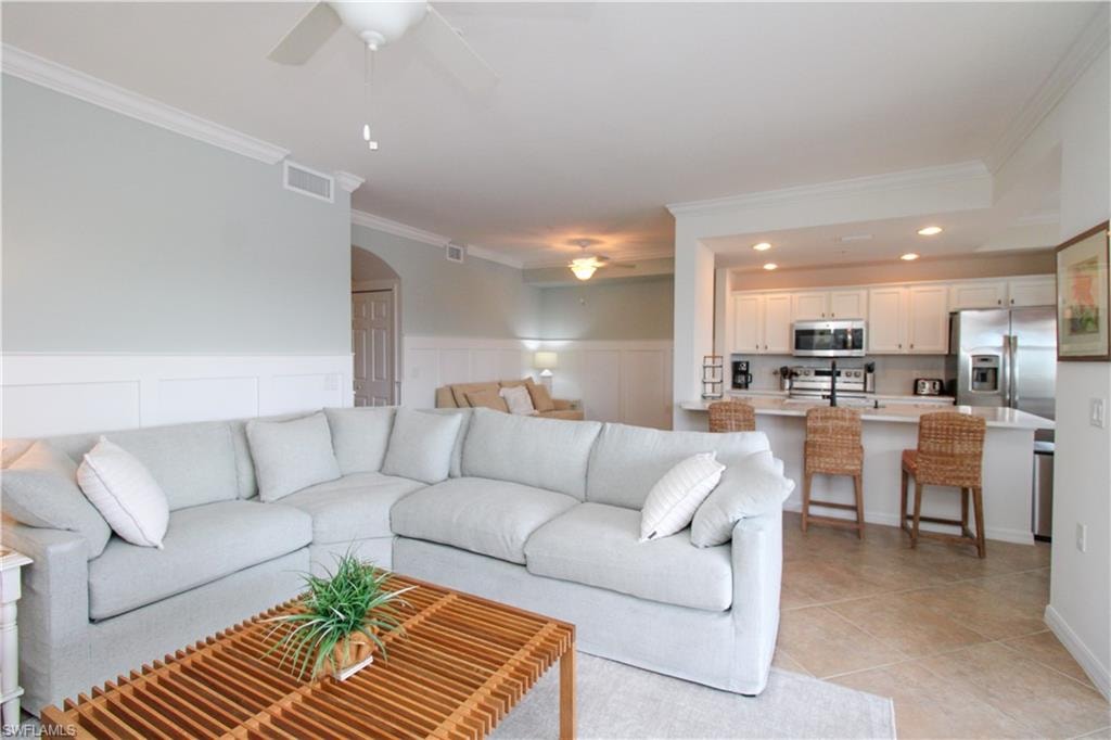 Living room with ceiling fan, light tile patterned flooring, and ornamental molding