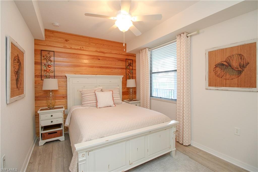 Bedroom with wood walls, ceiling fan, and light hardwood / wood-style floors