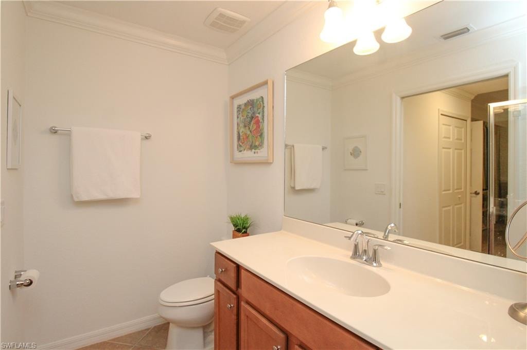 Bathroom with toilet, vanity, tile patterned floors, and ornamental molding