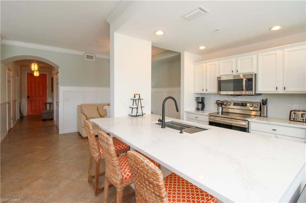 Kitchen featuring white cabinets, sink, a breakfast bar area, ornamental molding, and stainless steel appliances
