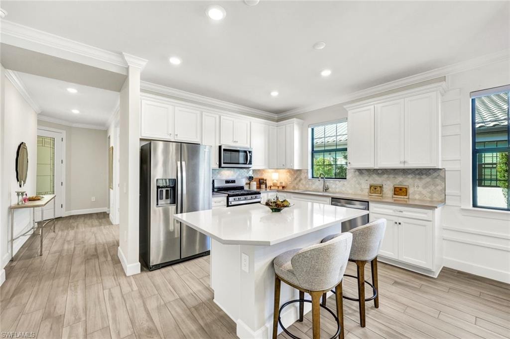 Kitchen featuring appliances with stainless steel finishes, white cabinetry, a kitchen bar, light wood-type flooring, and a kitchen island