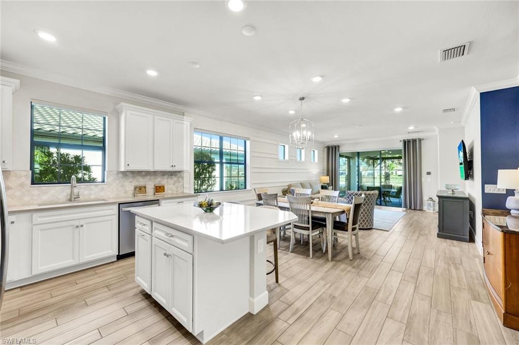 Kitchen with a kitchen bar, ornamental molding, white cabinets, a kitchen island, and hanging light fixtures
