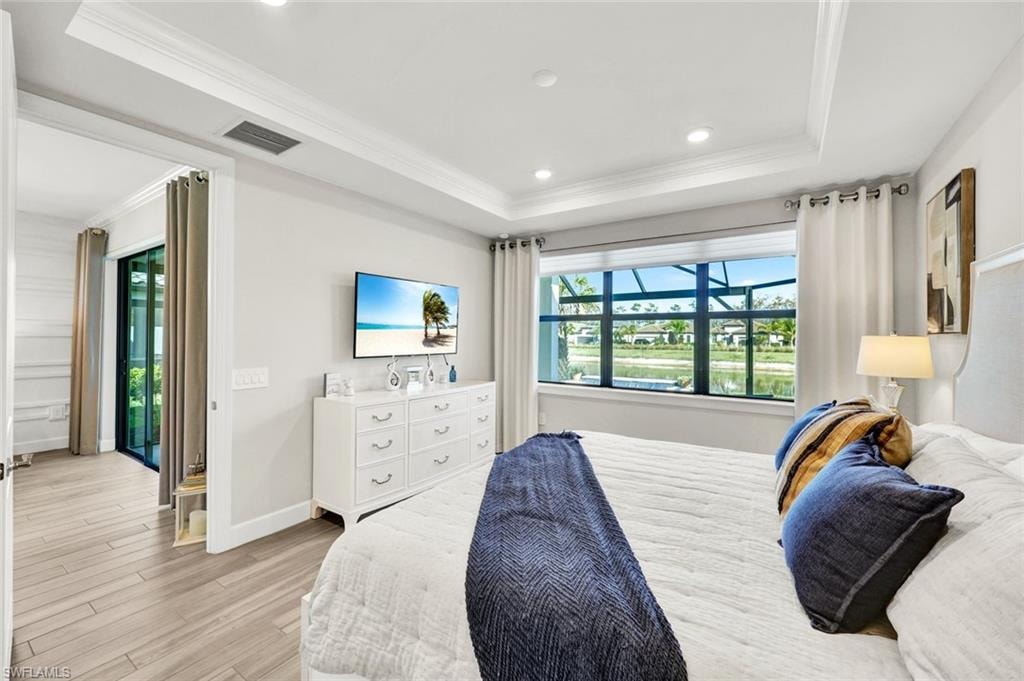 Bedroom featuring ornamental molding, light wood finished floors, recessed lighting, and a raised ceiling