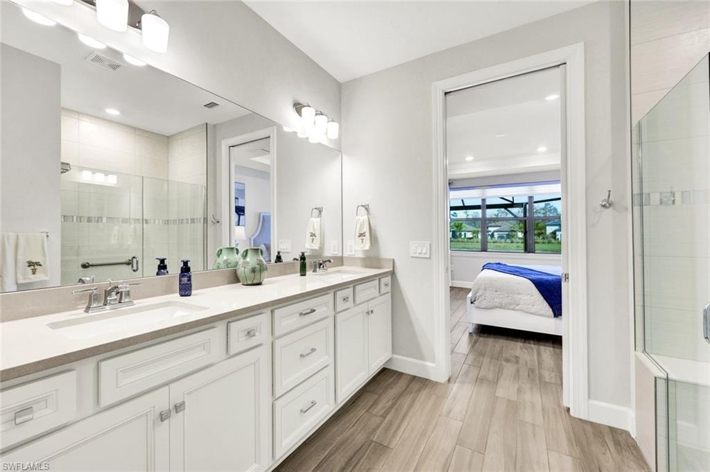 Bathroom featuring a stall shower, double vanity, connected bathroom, and wood finish floors