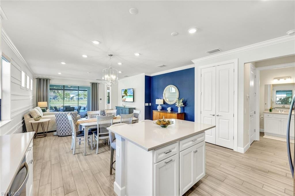 Kitchen with a kitchen island, a breakfast bar area, white cabinetry, wood tiled floors, and ornamental molding