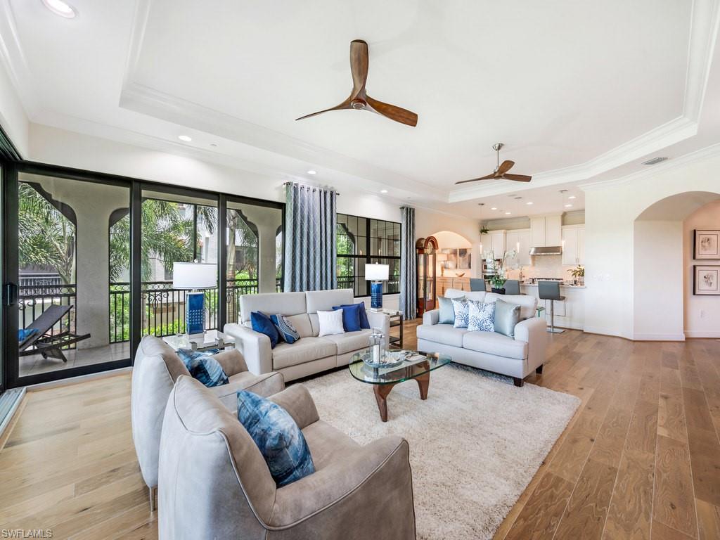 Living area with arched walkways, a raised ceiling, crown molding, hardwood / wood-style flooring, and recessed lighting