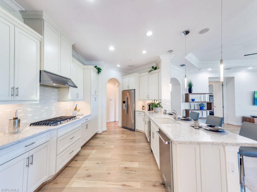 Kitchen with arched walkways, crown molding, light stone countertops, decorative backsplash, and light wood-type flooring