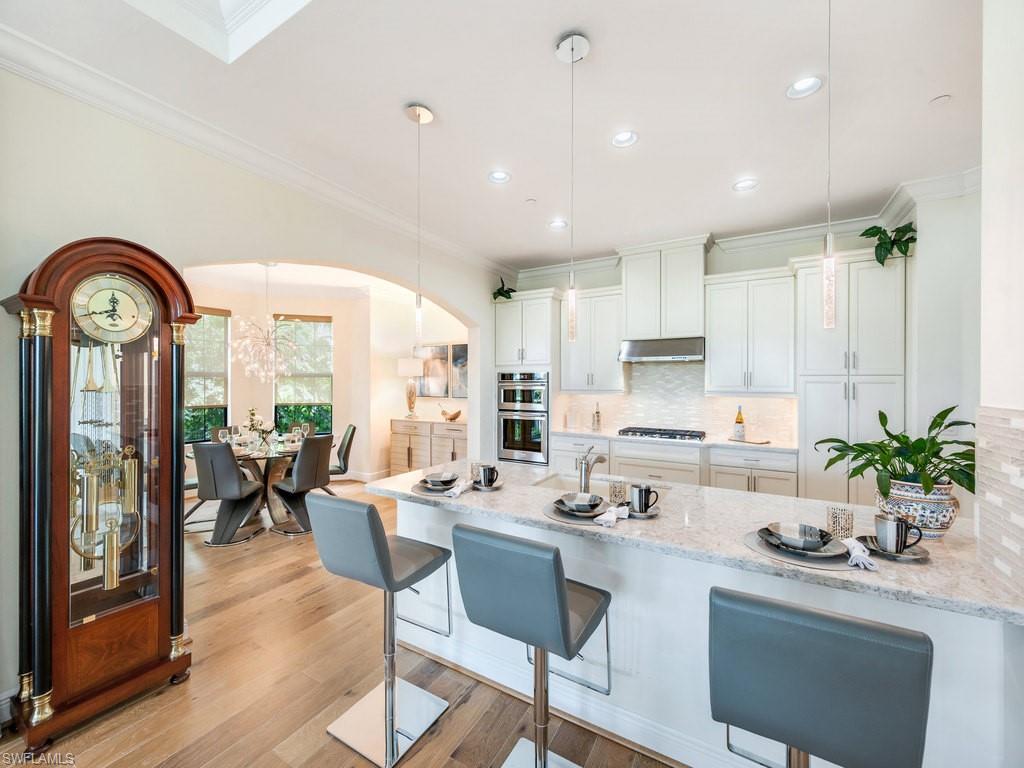 Kitchen featuring hanging light fixtures, a breakfast bar area, a peninsula, light stone counters, and crown molding
