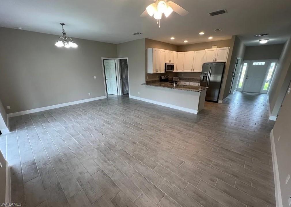Kitchen featuring open floor plan, fridge with ice dispenser, dark stone countertops, white cabinetry, and recessed lighting