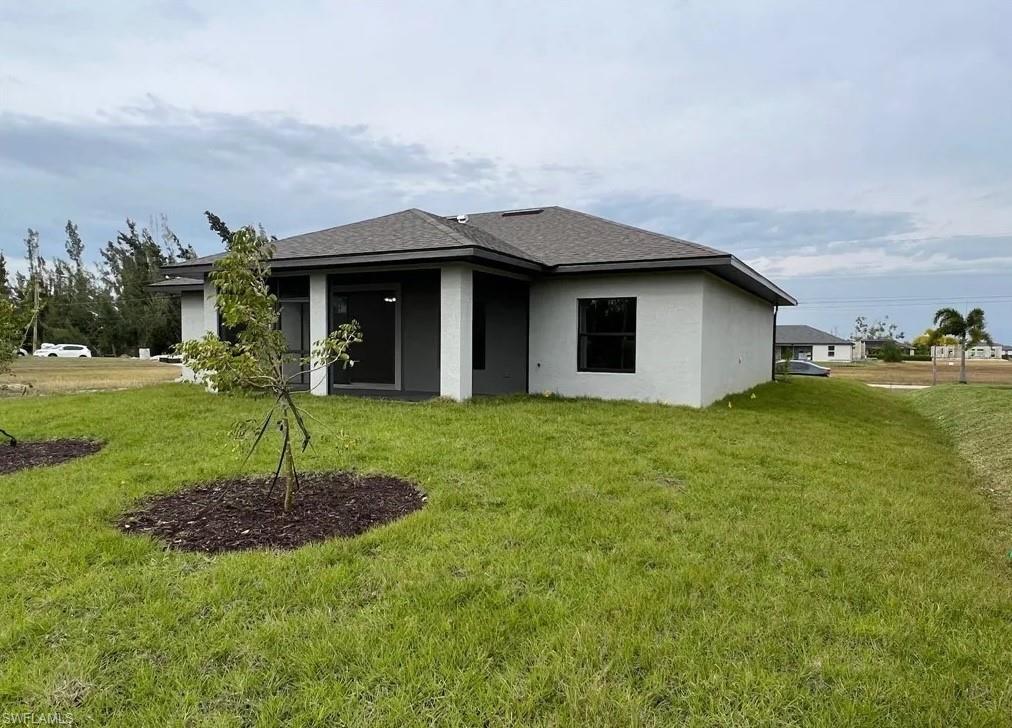 Rear view of property featuring a yard, stucco siding, roof with shingles, and a patio area