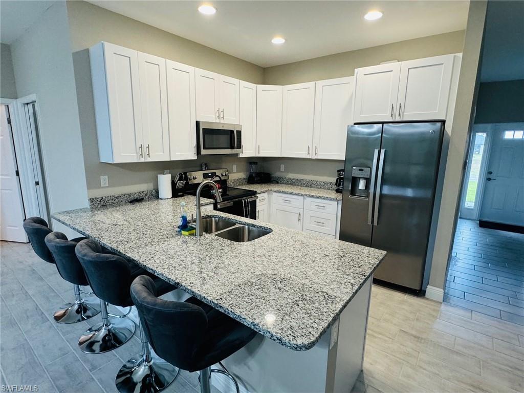 Kitchen with appliances with stainless steel finishes, a kitchen breakfast bar, a peninsula, white cabinetry, and light stone countertops