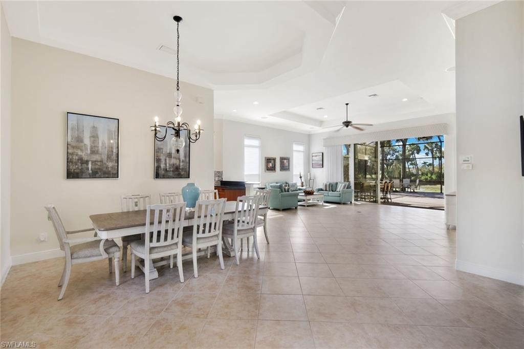Dining area featuring a tray ceiling, light tile patterned flooring, a chandelier, ceiling fan, and recessed lighting