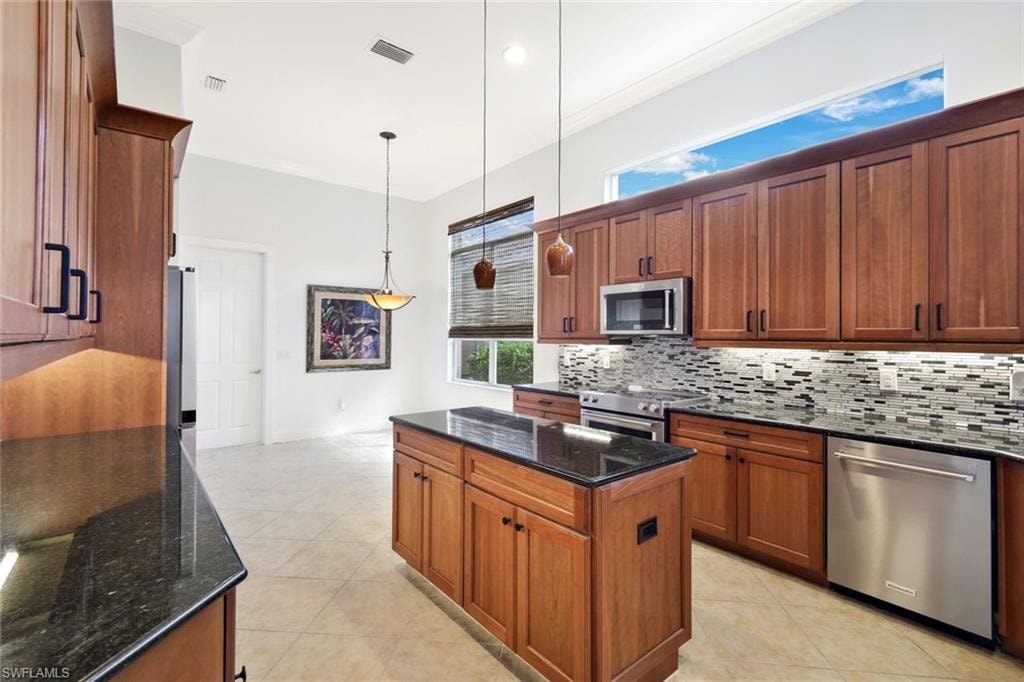 Kitchen featuring dark stone countertops, decorative light fixtures, stainless steel appliances, and brown cabinets