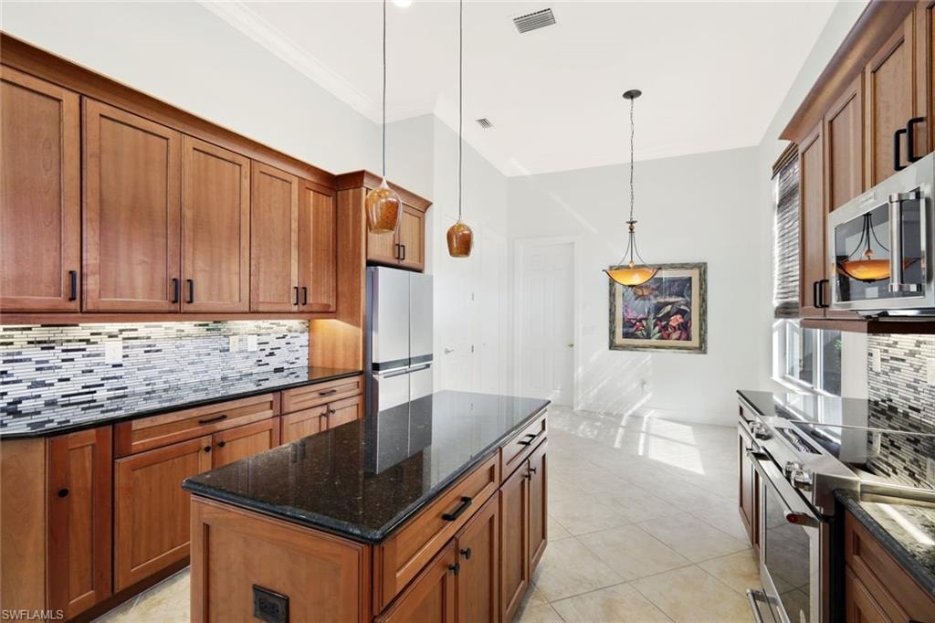Kitchen featuring decorative backsplash, brown cabinets, pendant lighting, stainless steel appliances, and dark stone counters