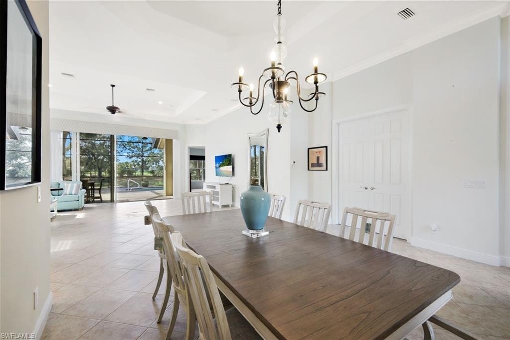 Dining space featuring a chandelier, a tray ceiling, light tile patterned floors, a ceiling fan, and ornamental molding
