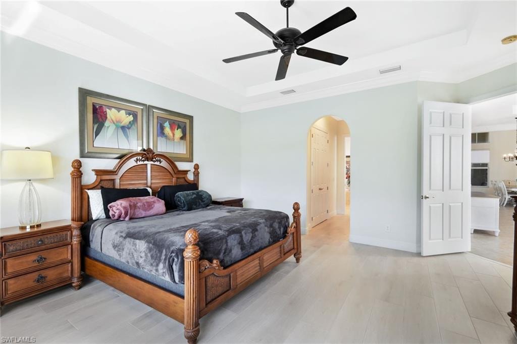 Bedroom with a raised ceiling, light wood-type flooring, a ceiling fan, and arched walkways