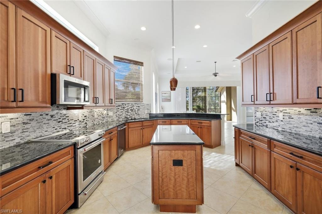 Kitchen featuring brown cabinets, stainless steel appliances, healthy amount of natural light, dark stone counters, and recessed lighting