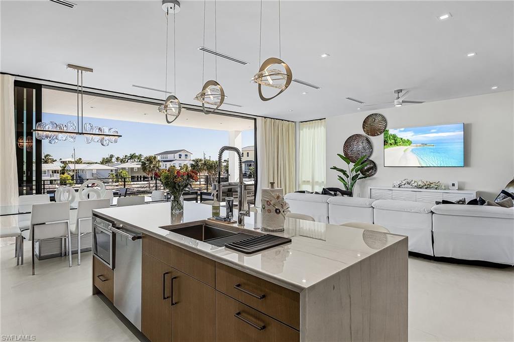 Kitchen featuring brown cabinetry, hanging light fixtures, modern cabinets, open floor plan, and a kitchen island with sink - Virtually Edited Image