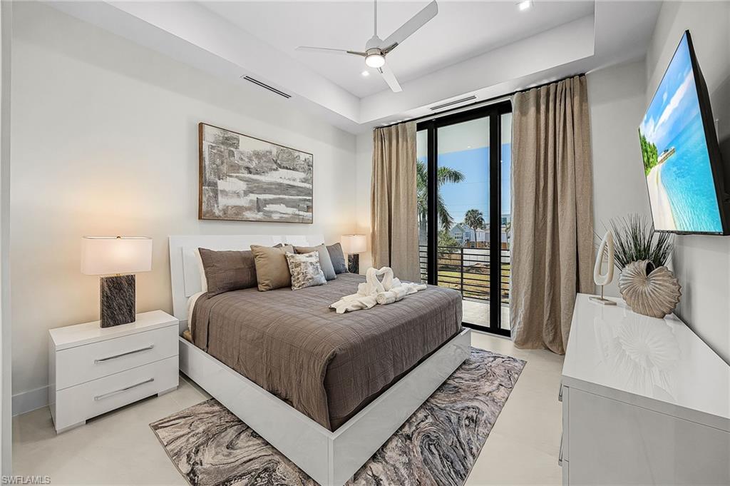 Bedroom featuring access to exterior, a ceiling fan, a raised ceiling, and recessed lighting - Virtually Edited Image