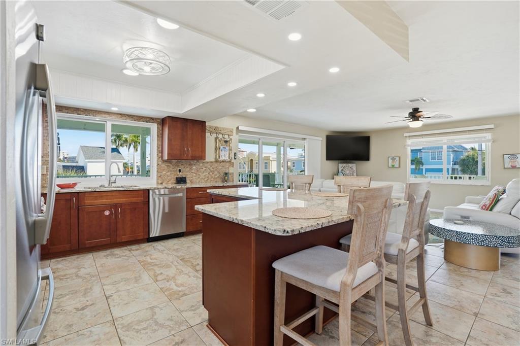 Kitchen featuring light stone countertops, appliances with stainless steel finishes, a center island, a breakfast bar, and recessed lighting - Virtually Edited Image