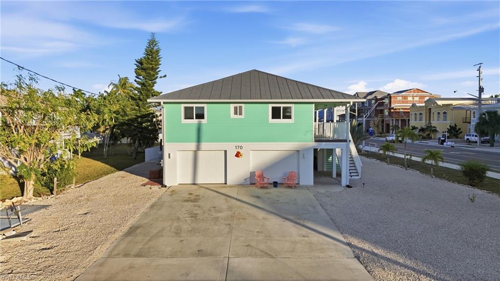 Back of property with driveway, stairs, a balcony, an attached garage, and a metal roof - Virtually Edited Image