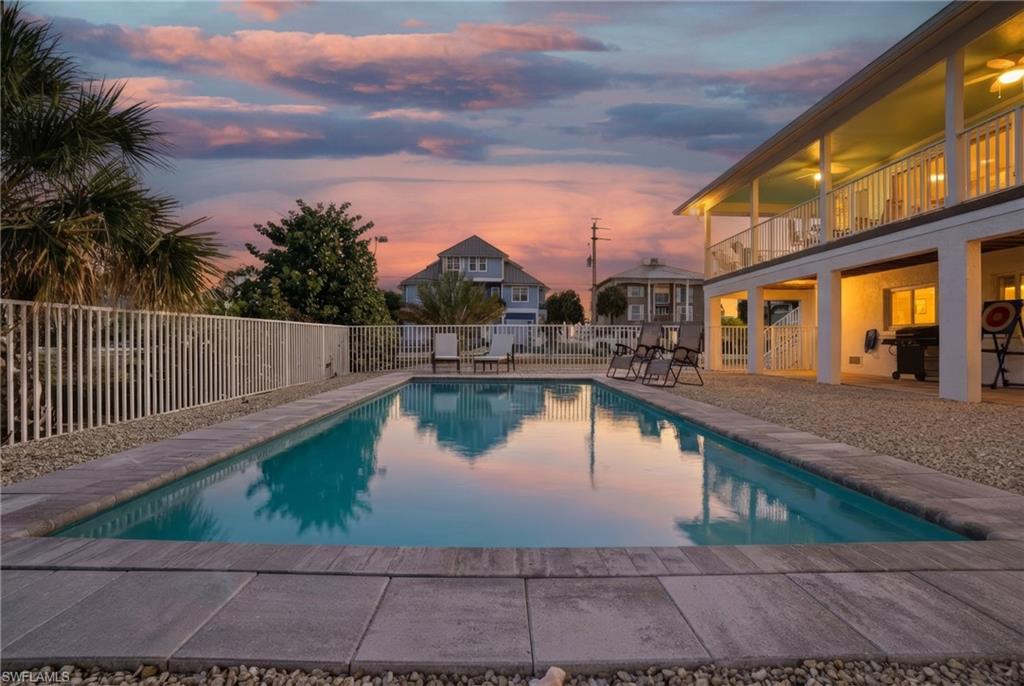Pool at dusk featuring a patio area, a fenced backyard, and a balcony - Virtually Edited Image