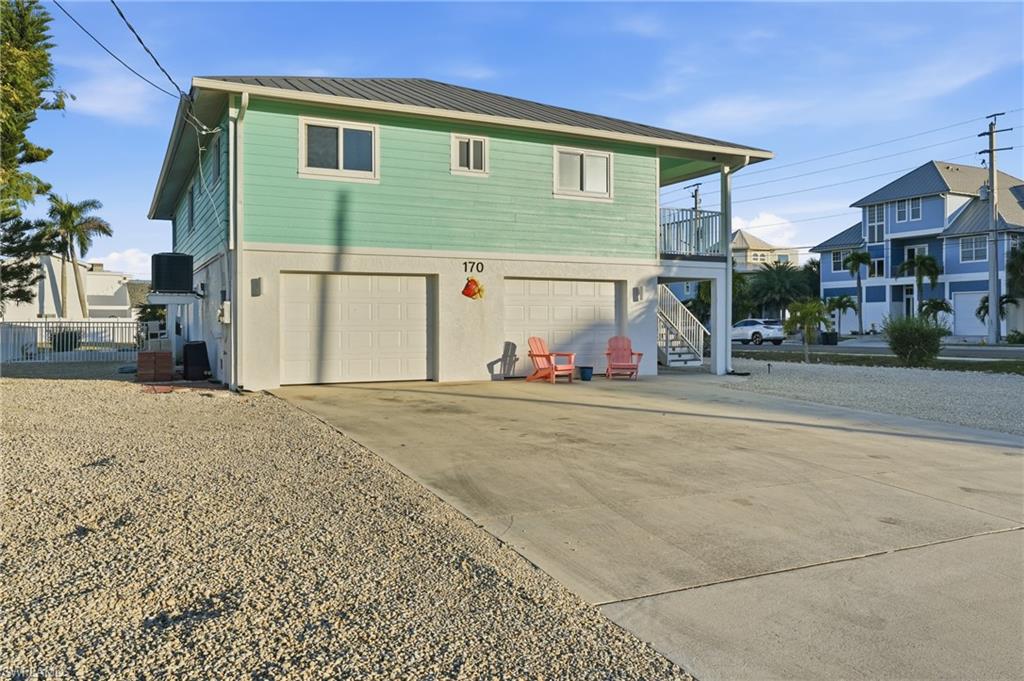 Rear view of house featuring driveway, a balcony, an attached garage, a metal roof, and stairs - Virtually Edited Image