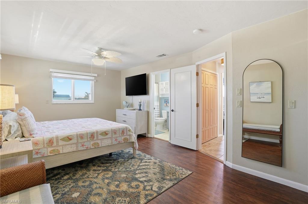 Bedroom featuring dark wood-type flooring, ceiling fan, and ensuite bathroom - Virtually Edited Image