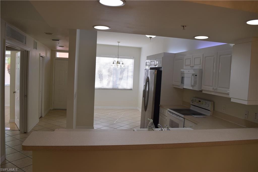 Kitchen featuring white cabinetry, white appliances, light countertops, light tile patterned flooring, and hanging light fixtures