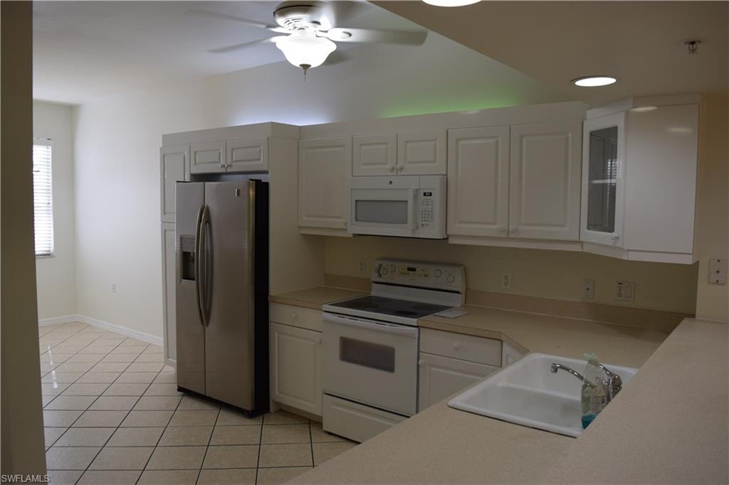 Kitchen with white appliances, light countertops, a ceiling fan, light tile patterned floors, and white cabinets