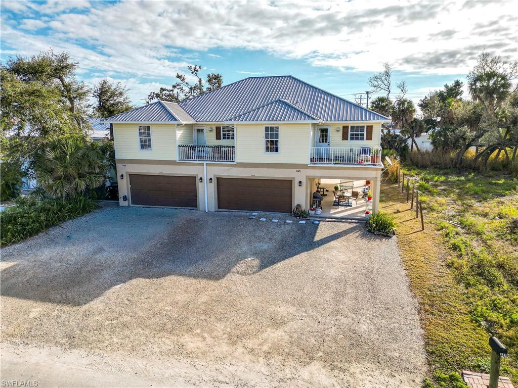 Coastal home featuring driveway, a balcony, a metal roof, and an attached garage